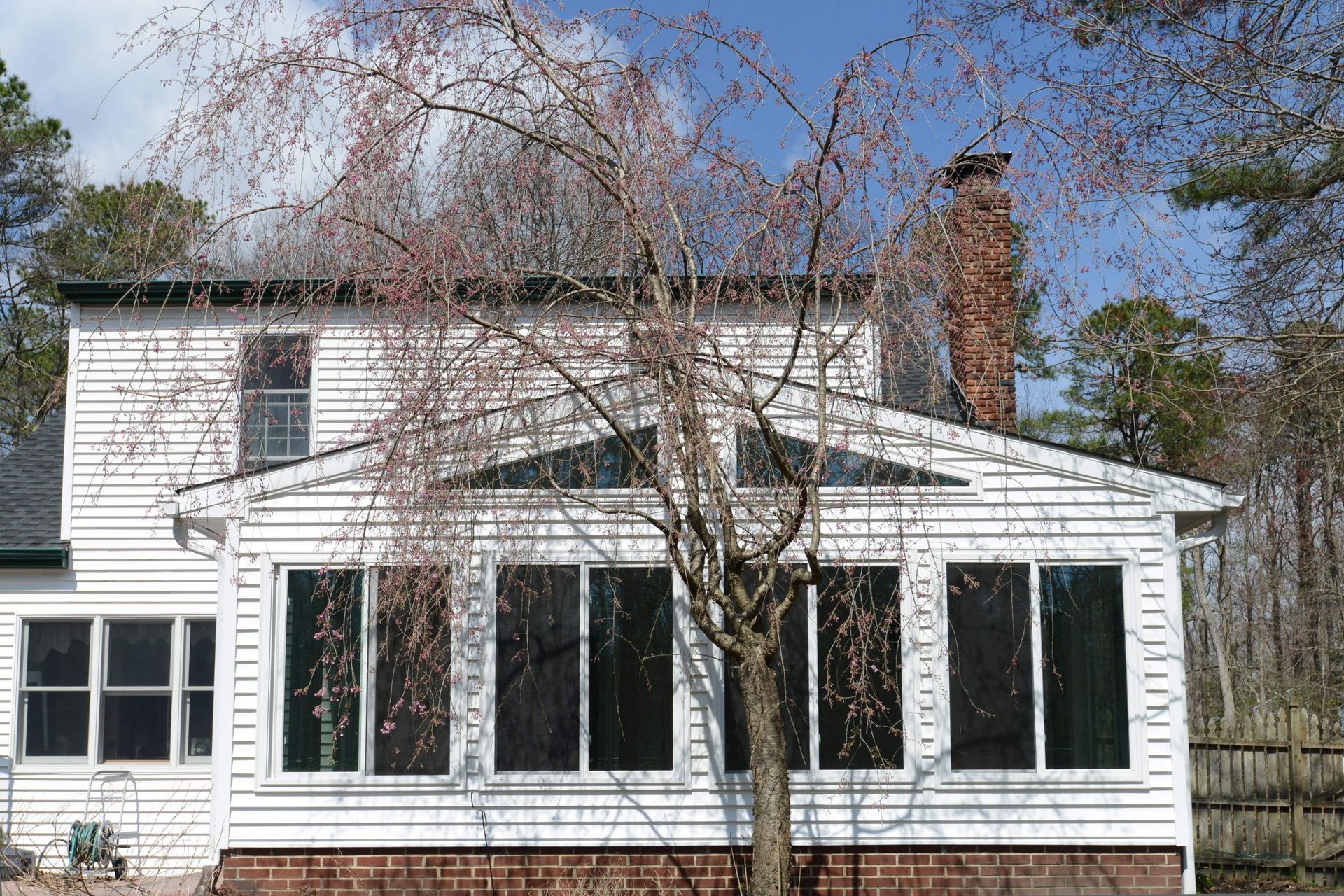 A two-story white house with a sunroom addition and a prominent weeping tree in the foreground.