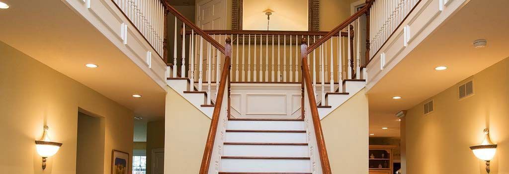 A grand, two-story foyer featuring a central wooden staircase with white balusters leading to an upper landing.