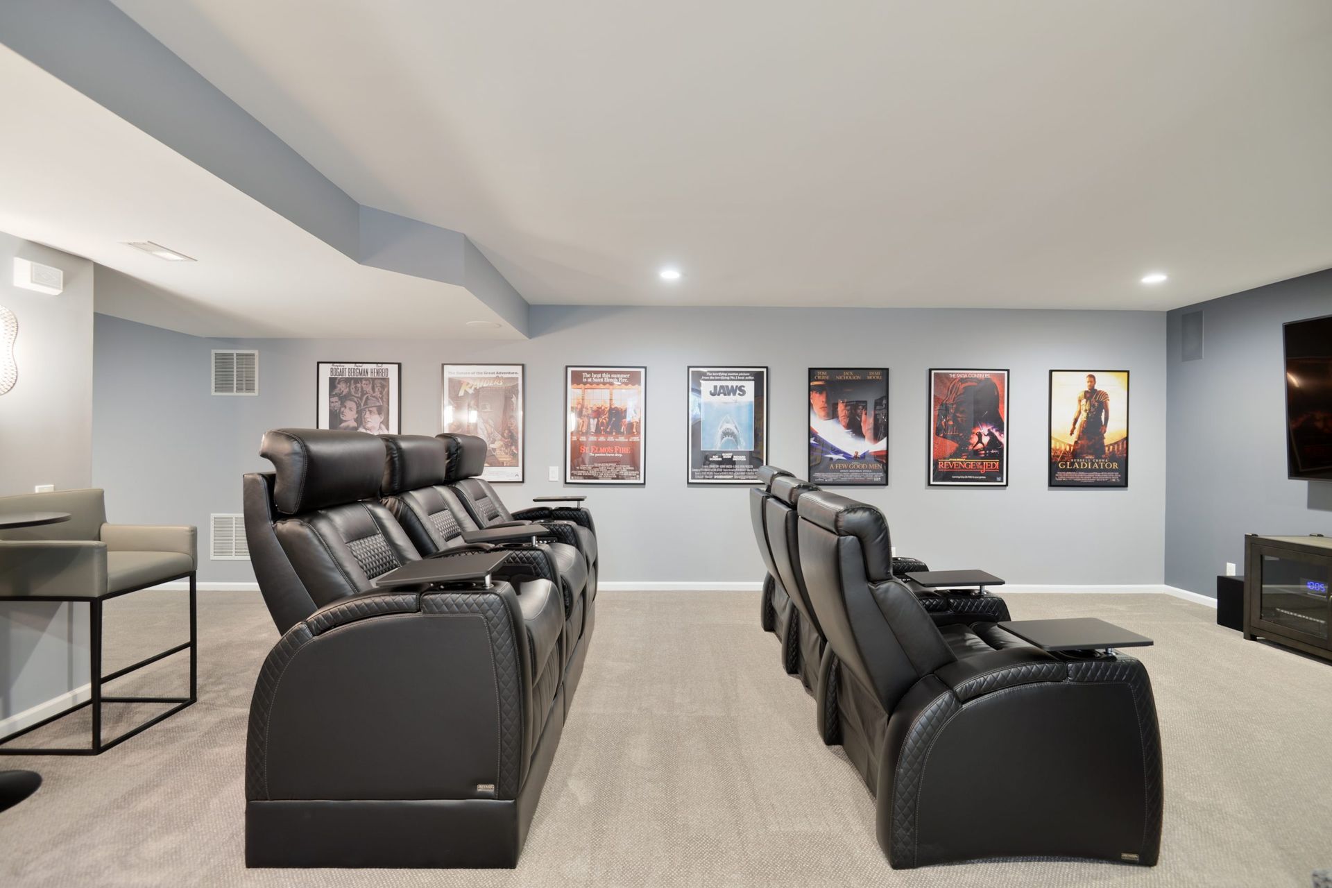 Home theater with two rows of black leather reclining seats, carpeted floor, and framed movie posters on a blue wall.