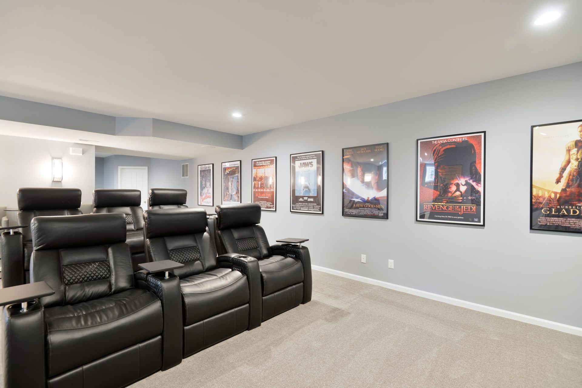 A basement home theater with rows of black leather recliners and framed movie posters lining the gray wall.