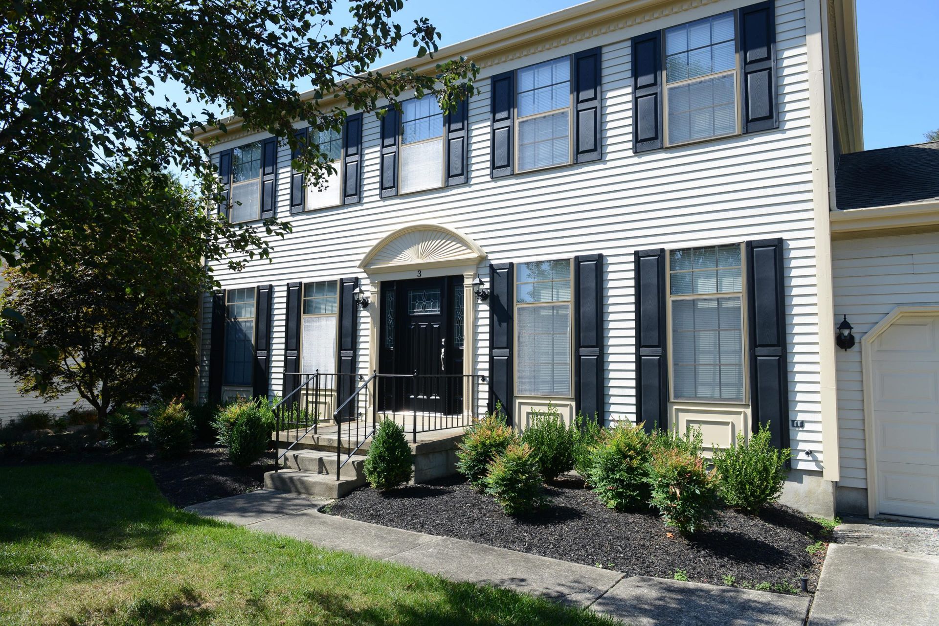 A two-story colonial house with white horizontal siding, black shutters, a dark front door, and a manicured front garden.