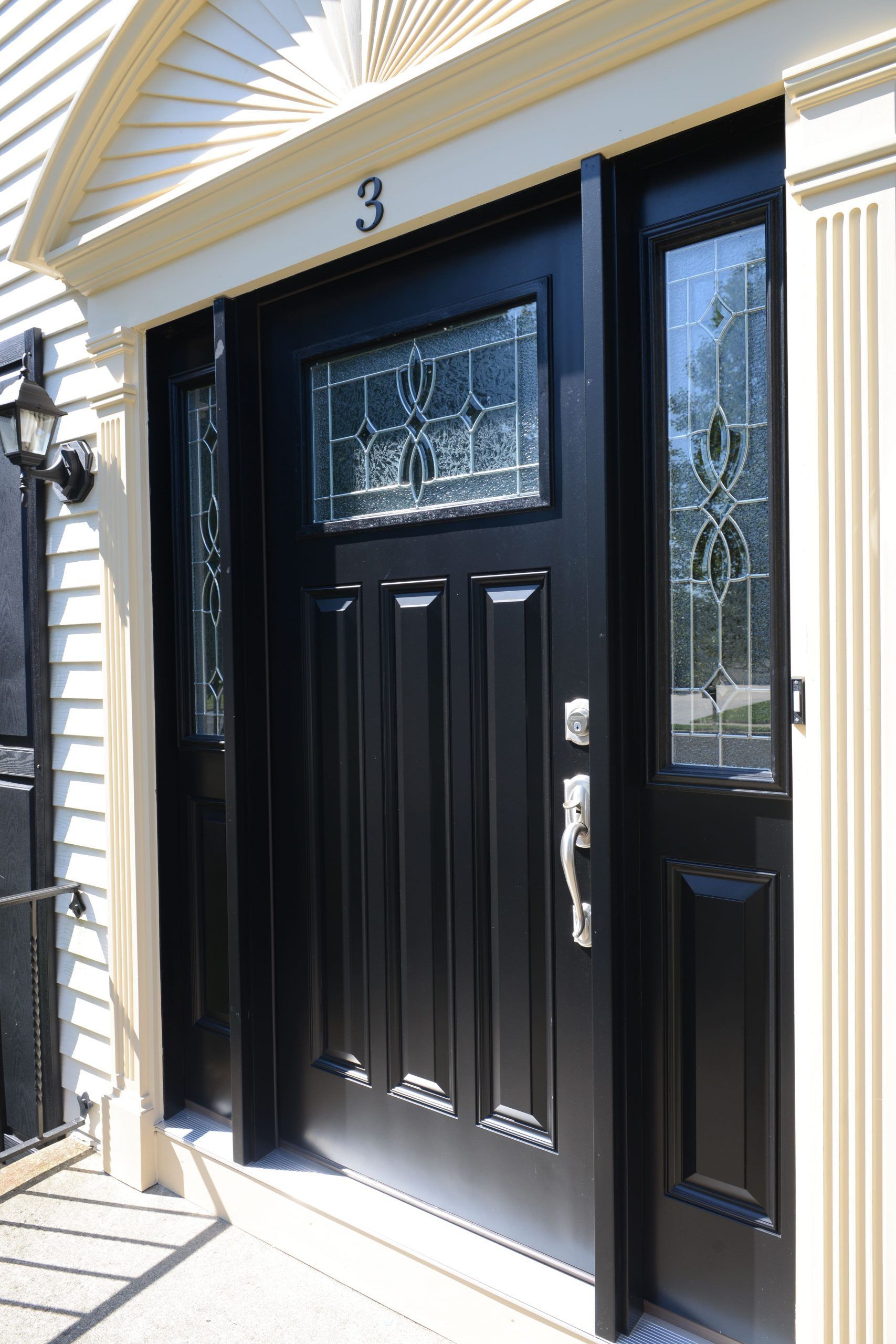 A black front door with glass panels, decorative moulding, and the number 3 above it, set in a light-colored frame.