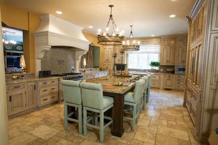 A spacious, traditional-style kitchen with a large granite island, light wood cabinetry, and teal upholstered bar stools.