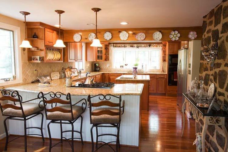 A bright kitchen with wooden cabinets, a granite island with three metal bar stools, and a stone accent wall.