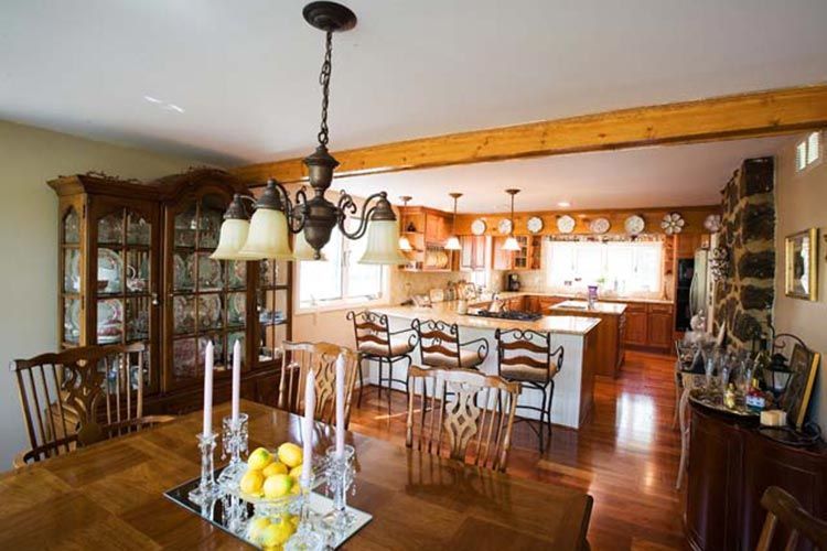 A dining room featuring a wooden table with candlesticks leads to an open-plan kitchen with a breakfast bar and wood cabinets.