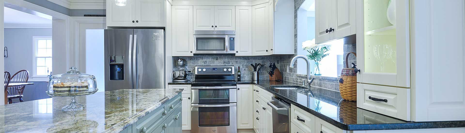 A bright kitchen with white cabinets, stainless steel appliances, dark granite countertops, and a large central island.