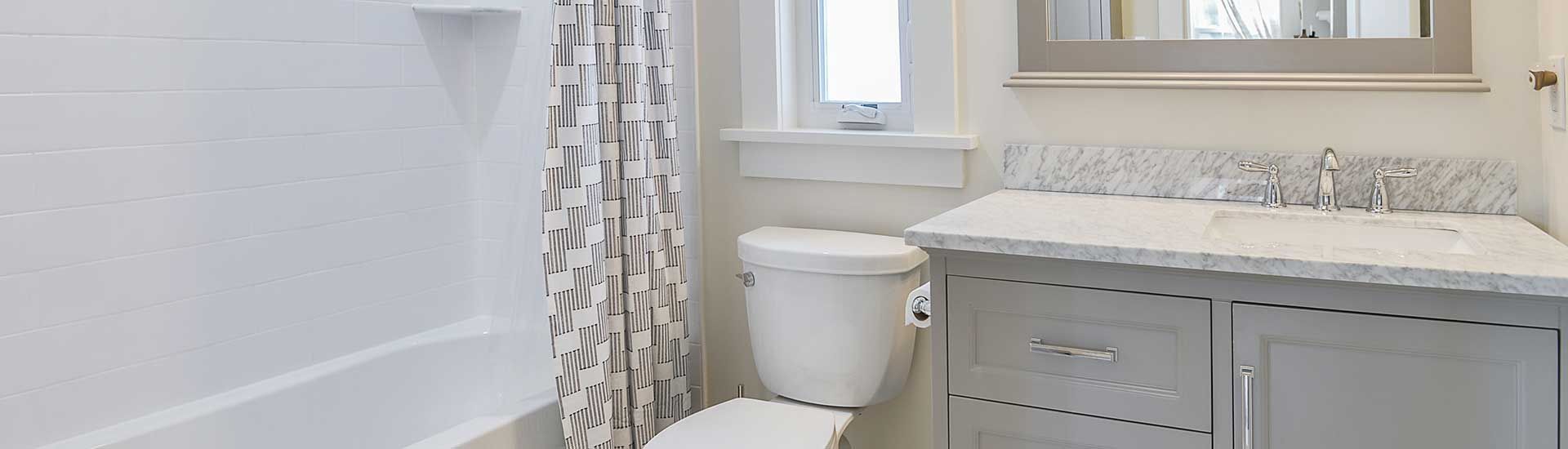 A brightly lit bathroom with a white shower, a gray vanity with a marble countertop, and a patterned shower curtain.
