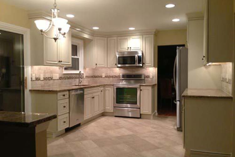A modern U-shaped kitchen with cream cabinets, stainless steel appliances, a tile backsplash, and light tile flooring.