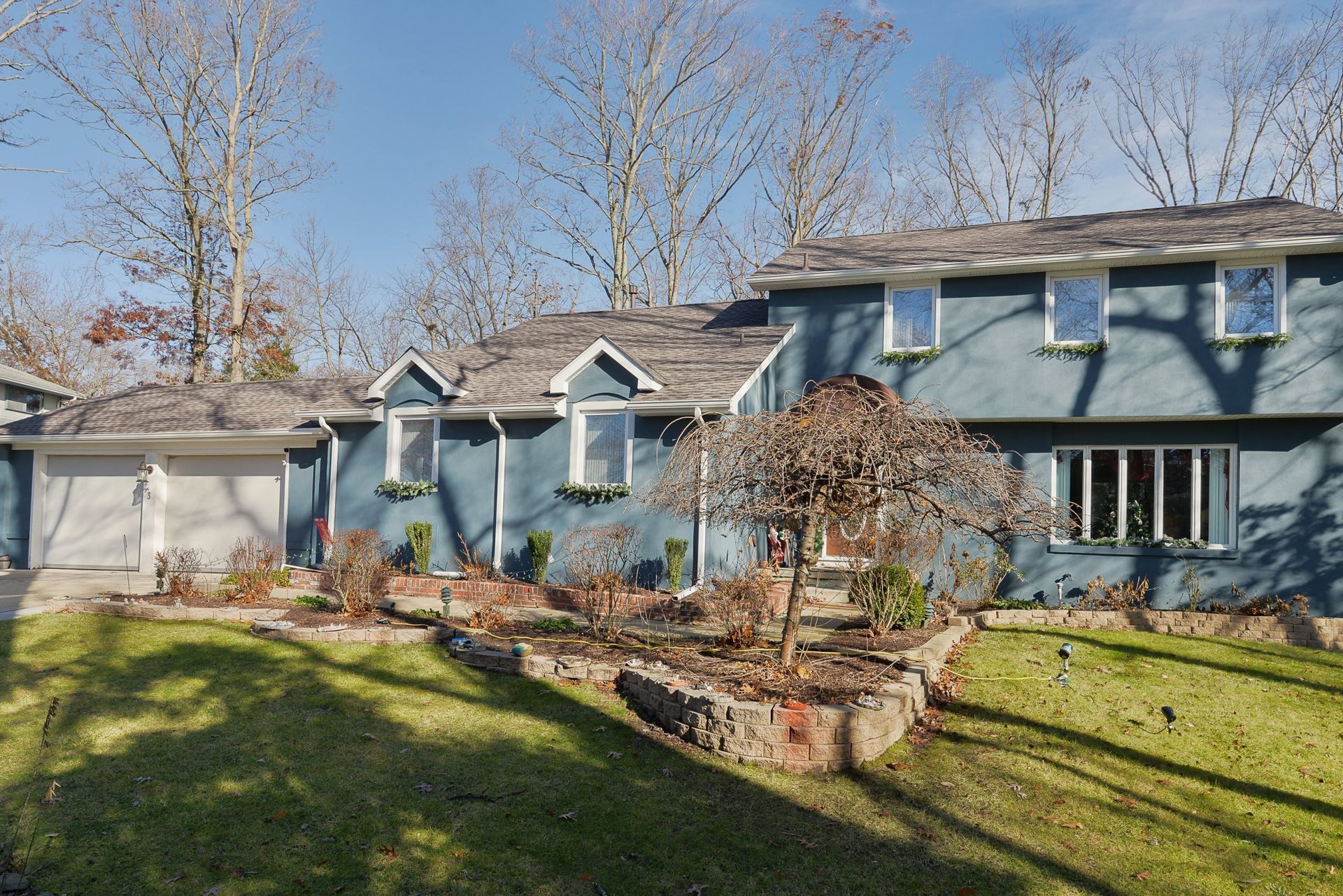 A blue, two-story house with a wooden shingle roof, two garage doors, and a terraced rock garden in the front yard.