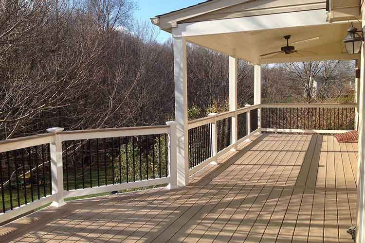 A wooden deck with white railings and a covered porch area overlooking bare trees in autumn.