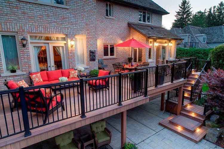 A multi-level wood deck attached to a brick house, featuring outdoor seating, a red umbrella, and stairs lit by LED lights.