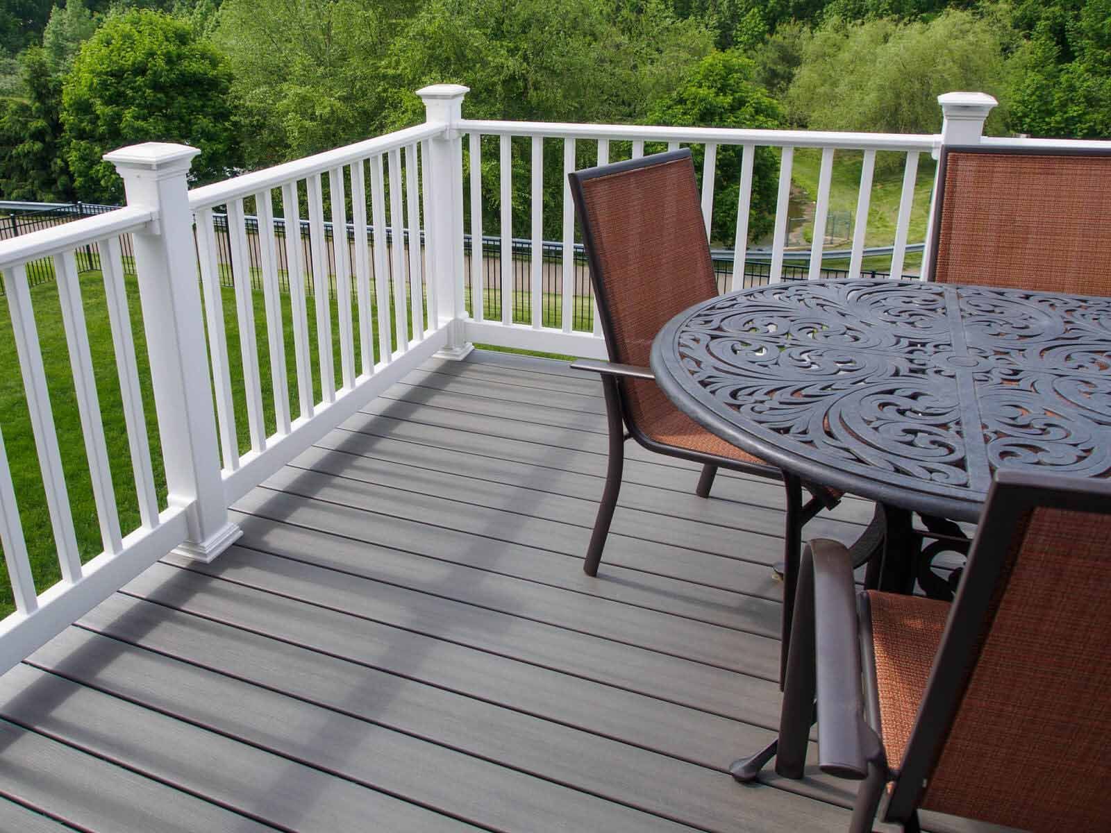 An outdoor deck with gray composite flooring, white railings, and a patio table with two brown chairs.