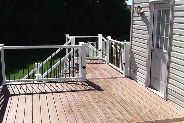 A wooden deck with white railings and a staircase leading down to a yard, attached to a house with white siding and a door.