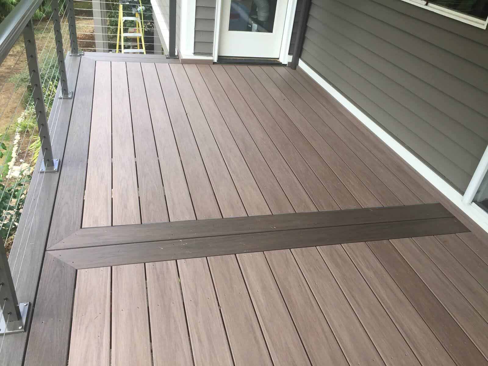 A multi-level outdoor deck featuring light brown planks with a dark brown accent strip and a metal railing.