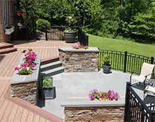 Multi-level outdoor patio with stone retaining walls, potted flowers, composite decking, and a black metal railing.