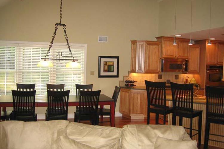 Dining room and kitchen area featuring wooden cabinets, a table with black chairs, and a pendant light fixture.