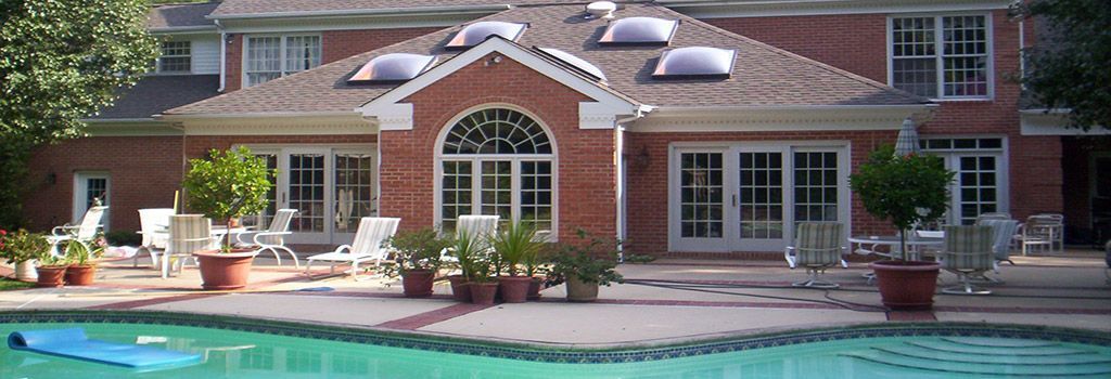 A red brick house with a large patio, potted plants, and outdoor furniture overlooking a swimming pool.