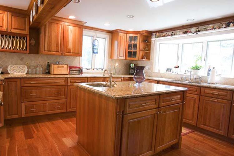 A bright kitchen with honey-toned wooden cabinets, a granite-topped island, and light hardwood floors.