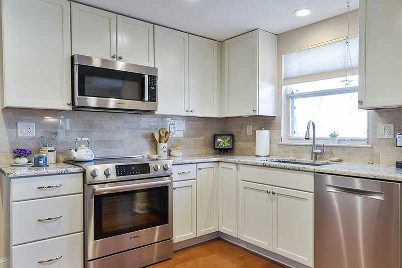 A modern kitchen featuring off-white cabinets, stainless steel appliances, speckled countertops, and a subway tile backsplash.