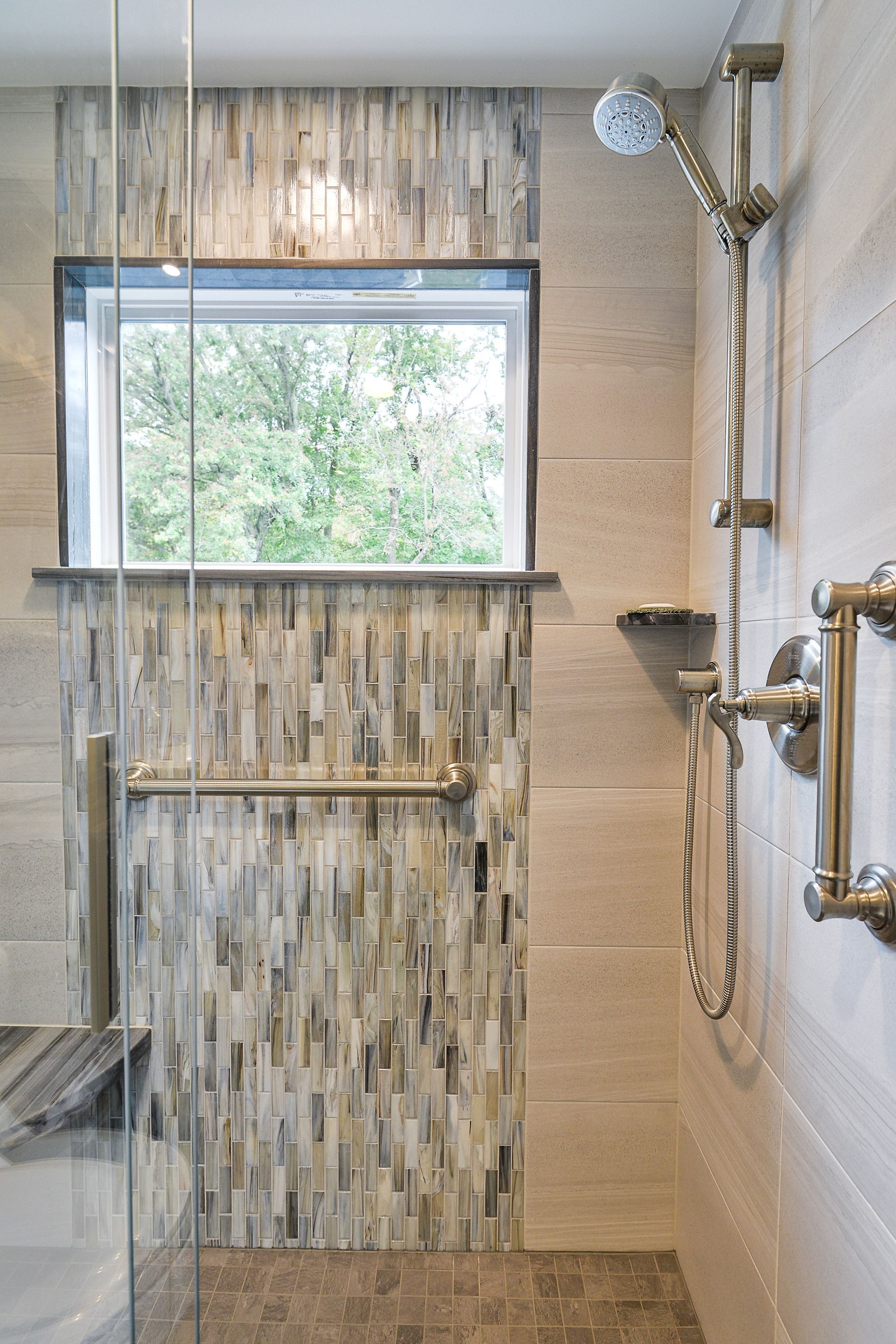Modern shower with a window, vertical stone mosaic tile accents, a metal grab bar, and bronze shower fixtures.