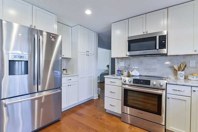 A modern kitchen featuring white cabinets, stainless steel appliances, and wood flooring.