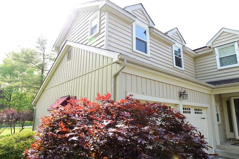 A multi-story beige home with light-colored vertical and horizontal siding, featuring a vibrant red Japanese maple tree.