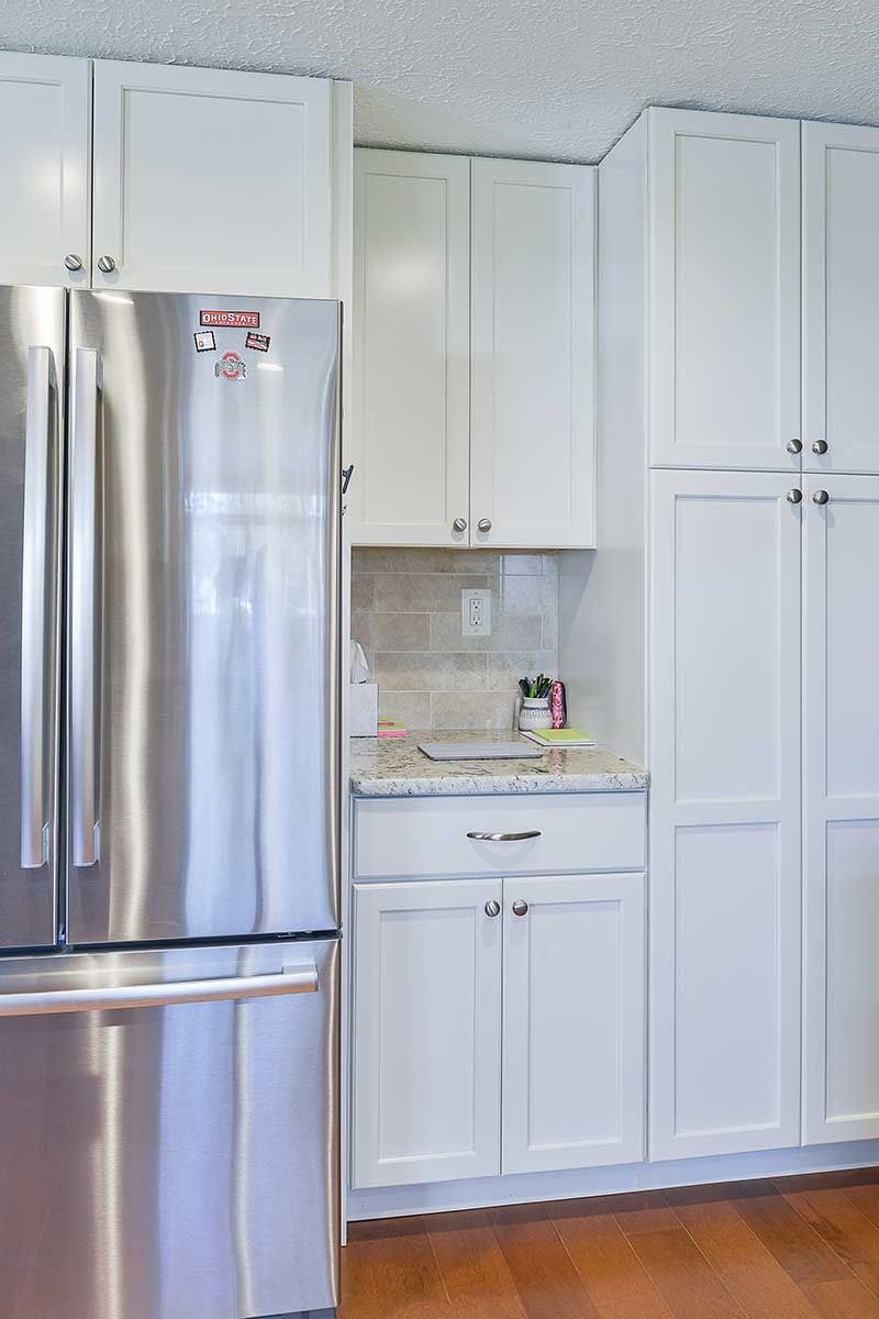 A stainless steel refrigerator next to white cabinets, a small countertop, and a tall pantry in a kitchen.