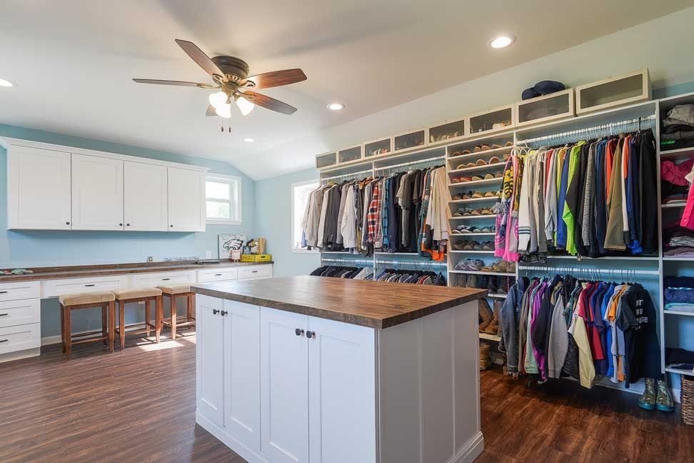 Spacious closet featuring white cabinets, a central wooden island, hanging clothing racks, and light blue walls.
