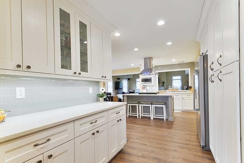 A bright, modern kitchen featuring white shaker cabinets, a long countertop, and a view into an adjacent dining area.