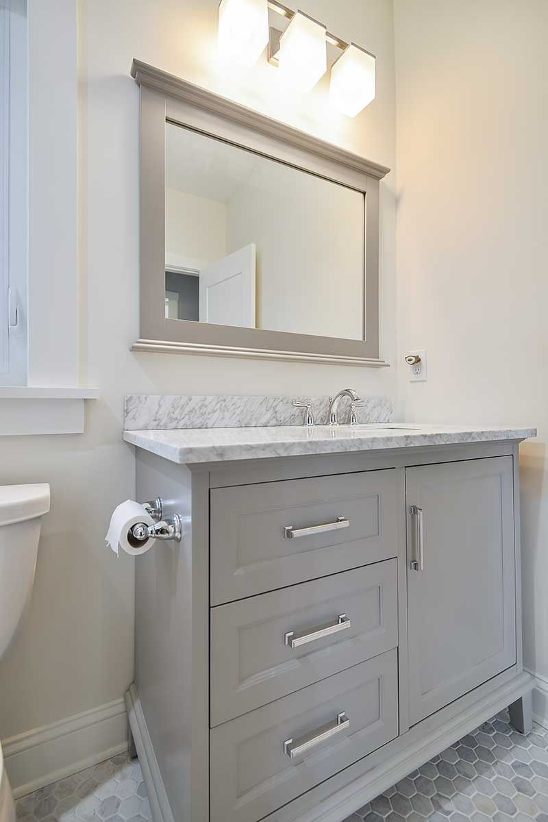 A grey bathroom vanity with a white marble countertop, mirror, and three-light fixture in a light-walled room.