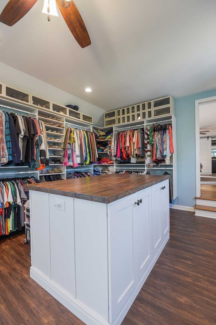 Walk-in closet with white cabinetry, a central wood-topped island, hanging clothes, and wood-look flooring.