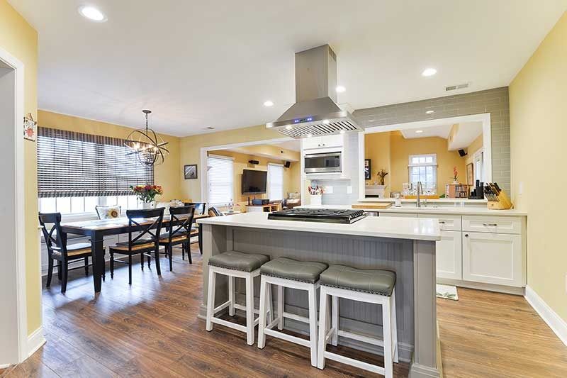 A kitchen featuring a central island with three stools, white cabinets, stainless steel appliances, and a dining area.