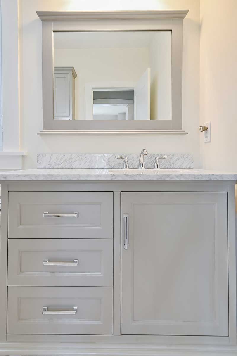 A gray bathroom vanity with three drawers and a cabinet door, topped with a marble countertop and a framed wall mirror.