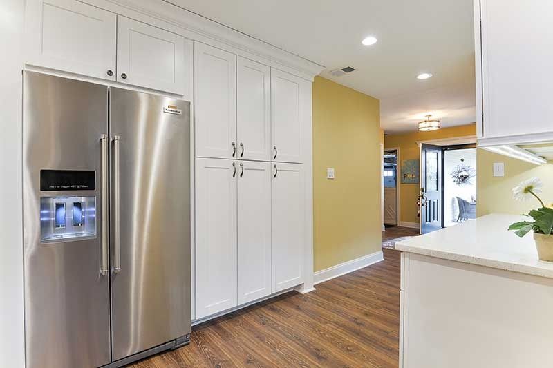 Stainless steel side-by-side refrigerator next to tall white pantry cabinets in a bright kitchen with yellow walls.