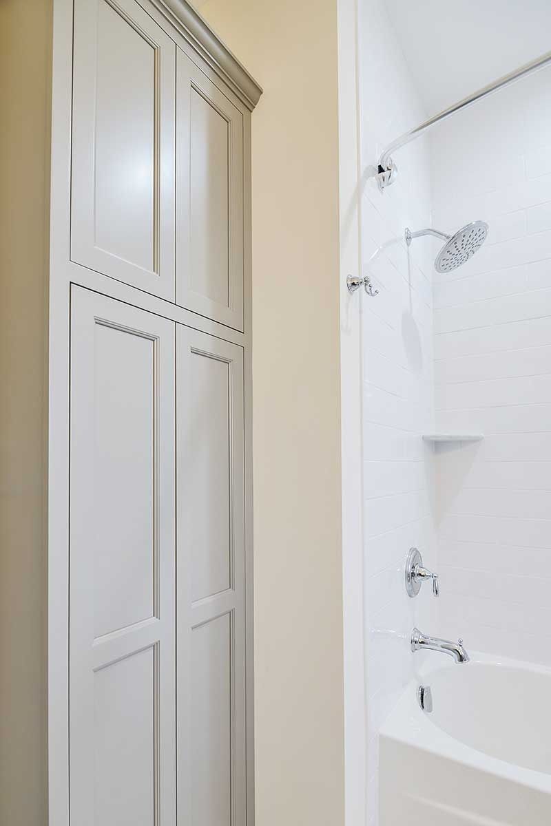 A tall, light-gray wooden storage cabinet sits beside a white bathtub and shower unit.