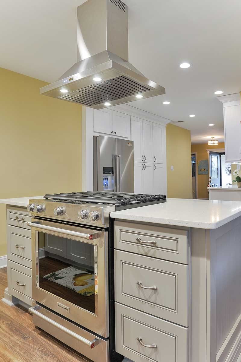 A modern kitchen island with a stainless steel gas stove and range hood, featuring light-toned cabinets and countertops.