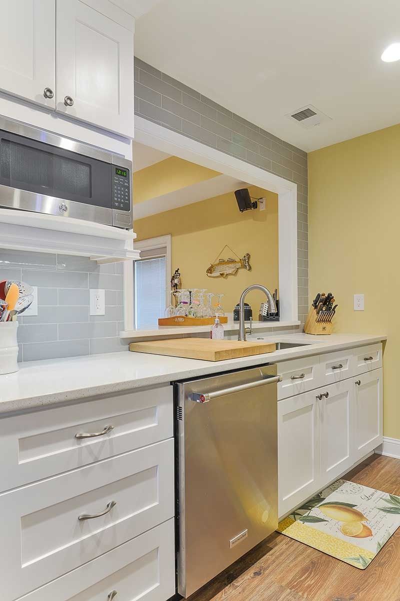 A kitchen with white cabinets, stainless steel dishwasher, grey subway tile backsplash, and light yellow walls.