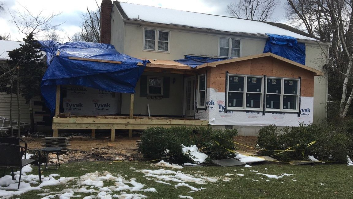 A two-story house undergoing exterior renovations with blue tarps, exposed wood framing, and snow on the ground.