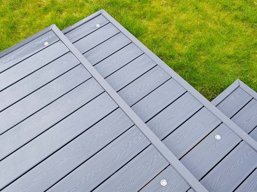A top-down view of gray composite decking stairs with integrated circular lights, set against a bright green grass lawn.
