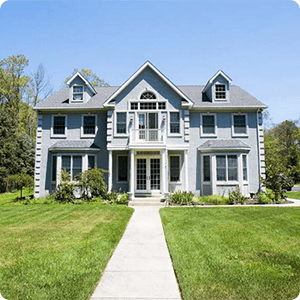 A two-story, light-blue house with a white trim, a centered balcony, and a straight walkway leading to the front door.