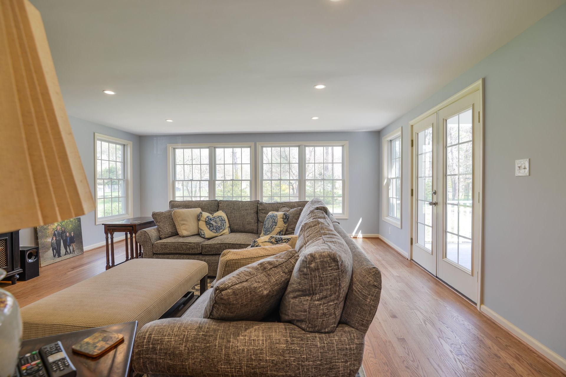 A bright living room with a large gray sectional sofa, a matching ottoman, and glass French doors leading outside.
