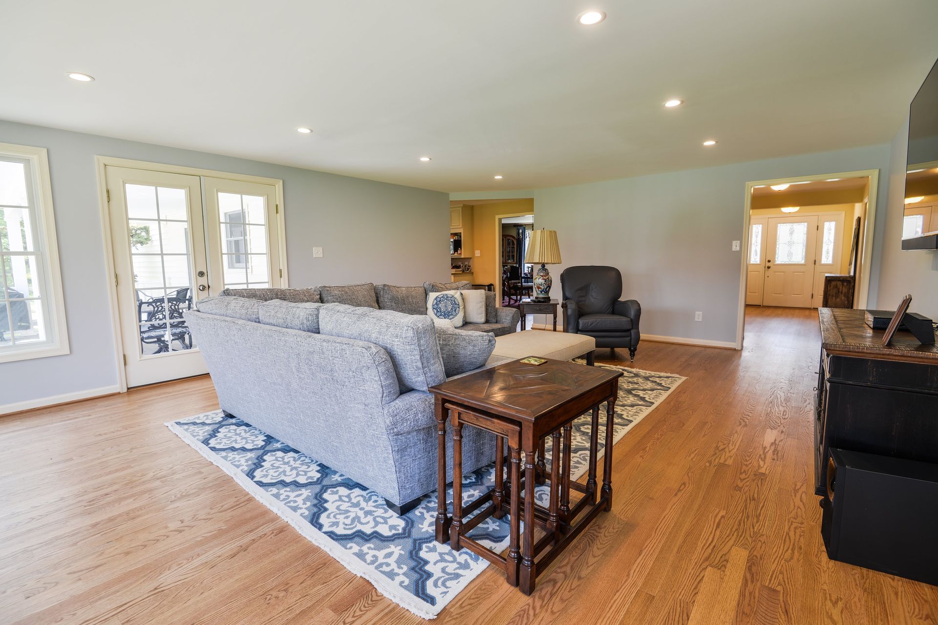 A spacious living room with hardwood floors, a blue patterned sofa on a matching rug, and a dark armchair.