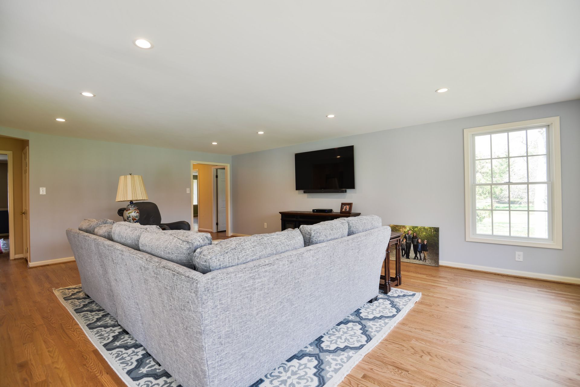 A living room with a large gray sectional sofa, hardwood floors, a television on a media console, and a large window.