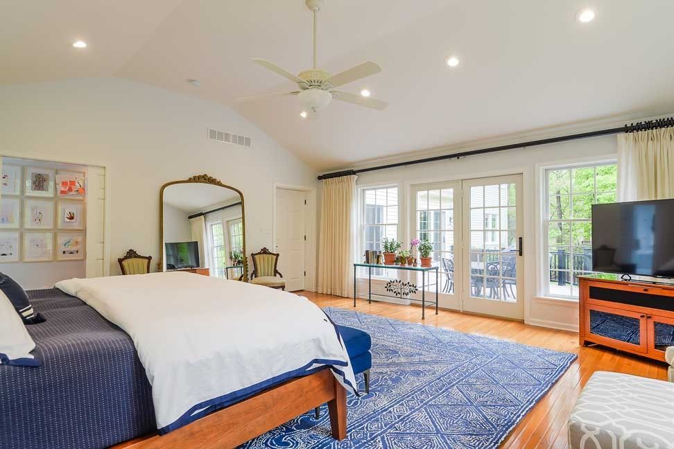 A bedroom with a king-sized bed, white walls, vaulted ceiling, large area rug, and patio doors leading to a backyard.