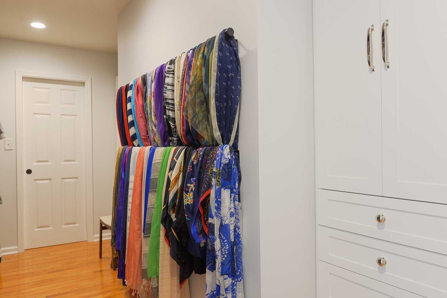 A collection of colorful scarves hangs neatly on a wall-mounted rack in a well-lit hallway next to white cabinetry.