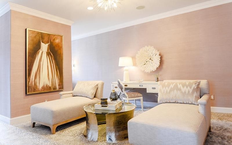 A chic, neutral-toned room featuring two beige chaise lounges, a gold-base coffee table, and a white vanity desk.