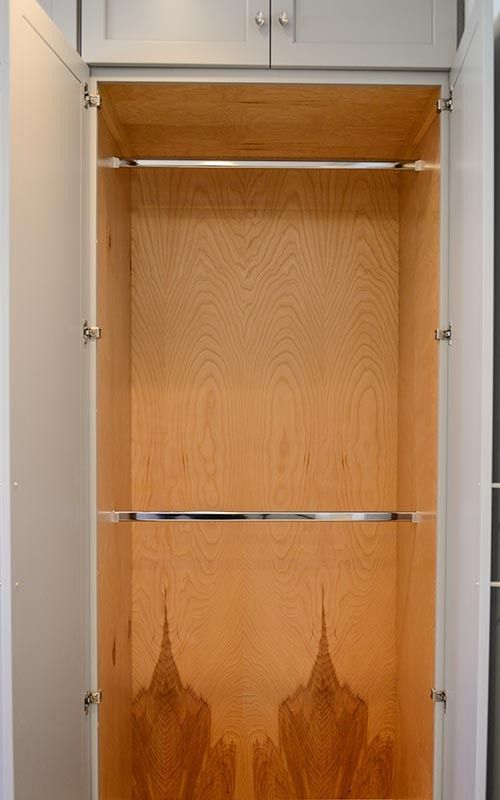 An open white cabinet with two horizontal metal rods mounted against a light wood-paneled interior.