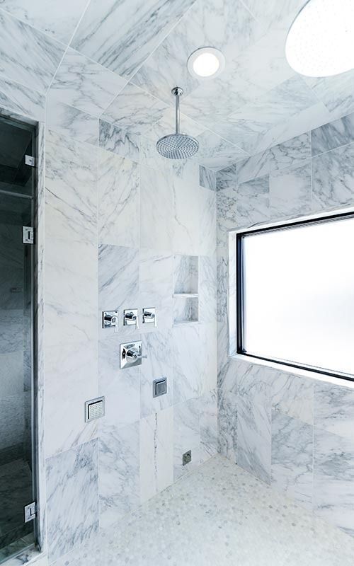 A luxurious, marble-tiled shower with a rainfall showerhead, wall-mounted fixtures, and a large frosted glass window.