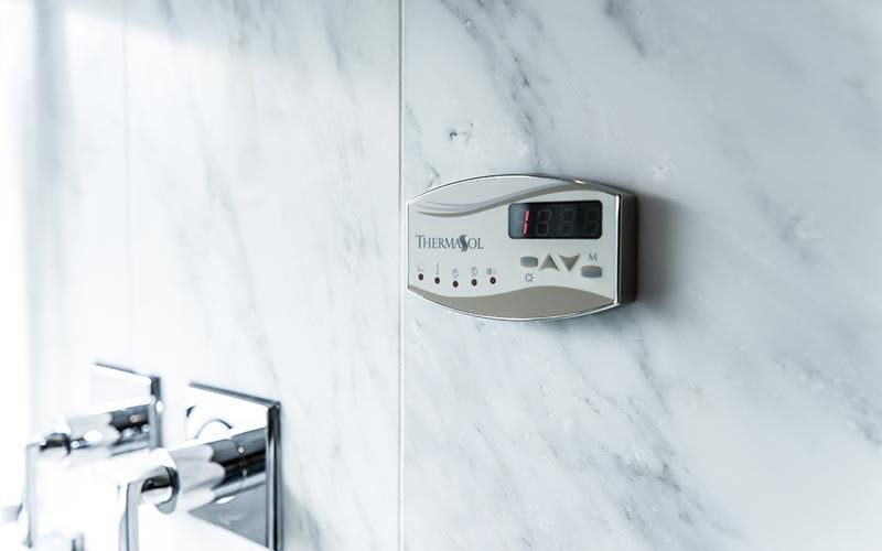 Digital Thermasol shower control panel mounted on a light gray marble wall next to a chrome shower fixture.