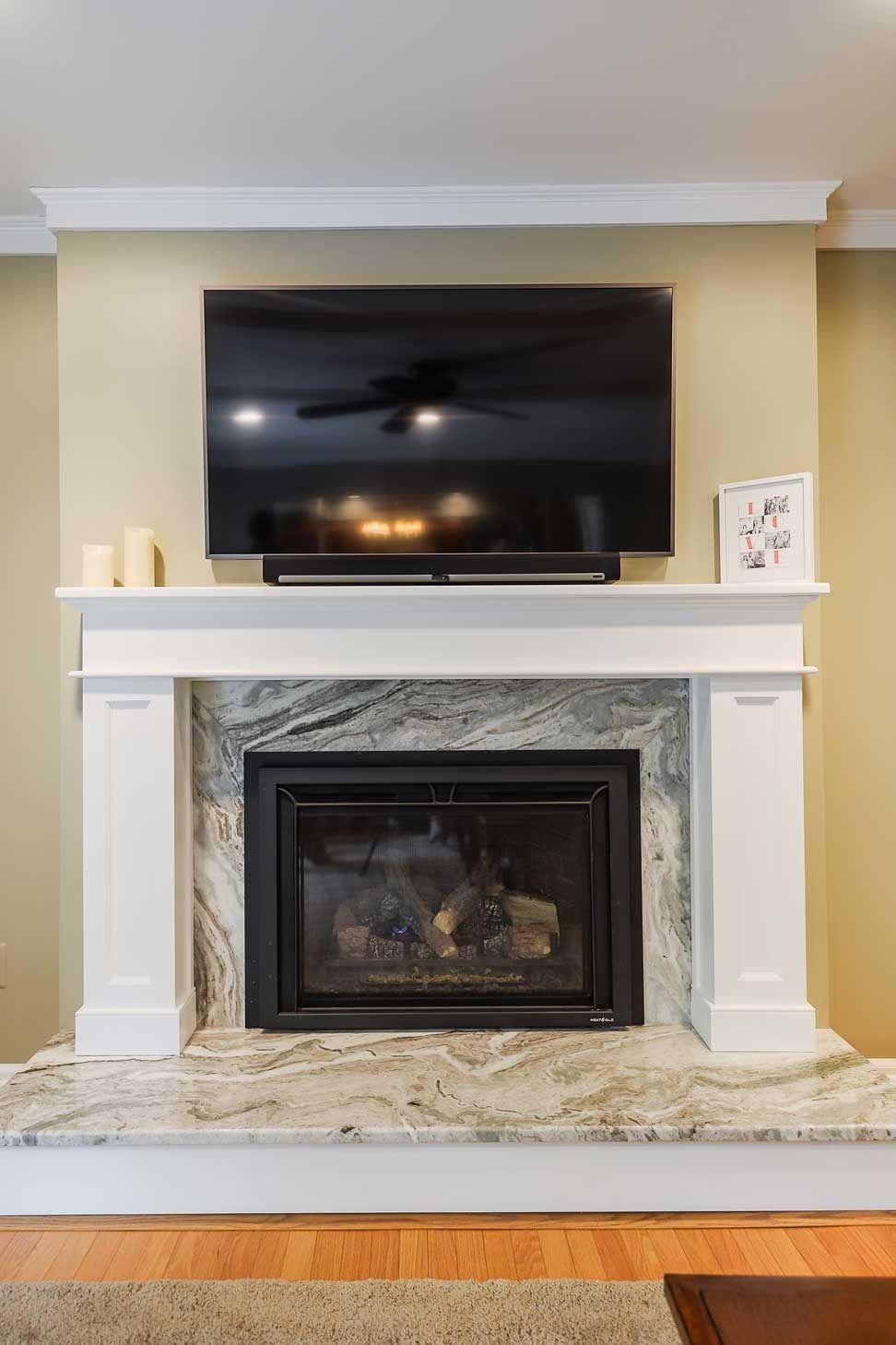 A wall-mounted TV sits above a white fireplace mantel with a granite stone surround and hearth.